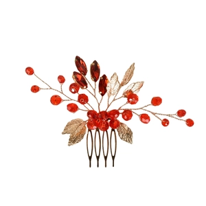 Macro shot of gold bridal hair comb with red crystal beads and metallic leaf details