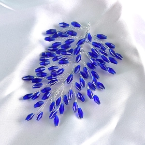 Detail of handcrafted blue crystal branch hair accessory on white silk fabric background