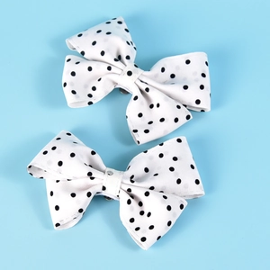 Close-up of white fabric shoe clips with black polka dot patterns in a bow design