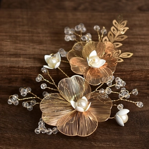 Close-up of golden wired flower bridal hair clip with white pearls on wood surface