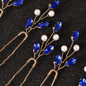 Macro detail of U-shaped hair pins with emerald blue stones and pearls on golden wire