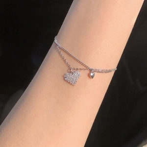 Close-up of double-layer bracelet featuring sparkling zircon heart and polished metal charms