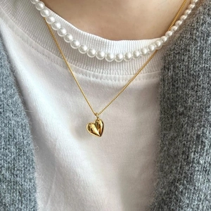 Détail d'un pendentif cœur doré et d'un collier de perles superposés sur un mannequin