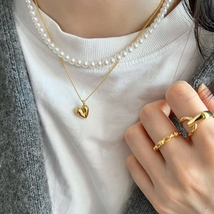 Gros plan du collier pendentif cœur doré, perles et bagues texturées sur le mannequin