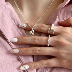 Détail du collier coeur en argent et bagues texturées portées à la main pour un look chic