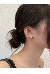 Détail d'une boucle d'oreille carrée en zircon noir et d'un anneau doré sur l'oreille