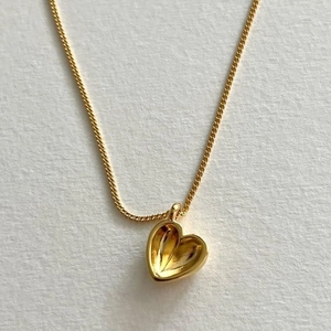 Vue macro du pendentif coeur 3D doré avec texture radiale et chaîne à maillons fins