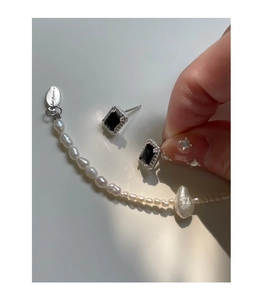 Détail de boucles d'oreilles en zircon noir et collier de perles baroques avec pendentif