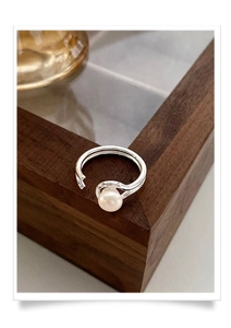 Detail of a minimalist double-layered silver ring with a glossy white pearl on wood