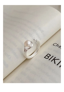 Detailed view of adjustable double-layer silver ring with white pearl on a book