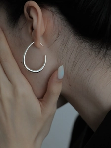 Dettaglio di orecchini a cerchio a goccia in argento lucido su modella stile minimal