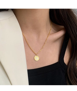 Detail view of gold rabbit coin necklace with asymmetric chain on white blazer