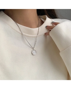 Detailed view of a silver rabbit coin pendant worn over a cream-colored sweater