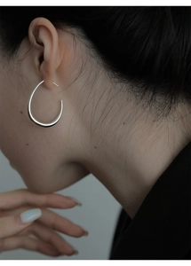 Dettaglio ravvicinato di orecchini geometrici ovali in argento lucido indossati da modella