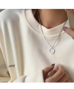 Detail of silver coin necklace with rabbit relief and textured chain on a model