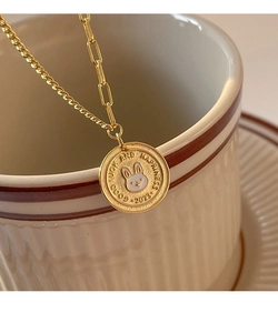 Macro detail of gold coin necklace with white enamel bunny and Good Luck engraving