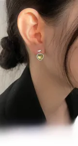 Close-up of heart-shaped cat-eye earrings with green gradient and bow detail on ear