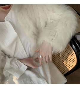Close-up of minimalist silver rings worn with a soft white faux fur cardigan and shirt