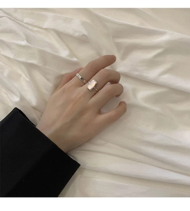 Close-up of minimalist silver shell ring set worn on hand with white fabric background