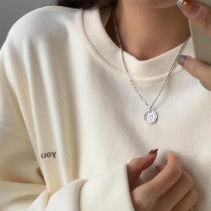 Minimalist silver rabbit coin necklace with embossed rabbit pendant on cozy cream sweater