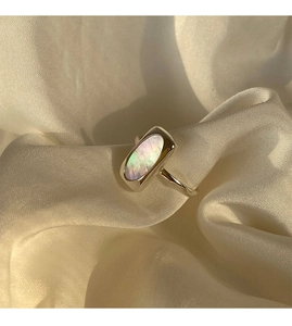 Detailed shot of a silver shell ring featuring iridescent inlay on beige silk fabric
