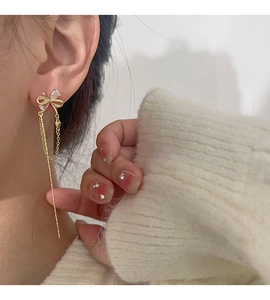 Close-up of golden bow earrings with long tassels and sparkling zircons on model