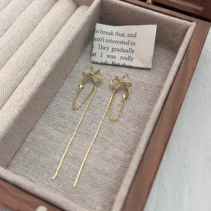 Detail of gold bow tassel earrings with crystals on a wooden jewelry display case