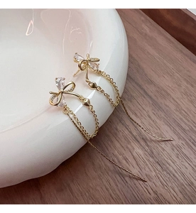 Detail of gold bow earrings with crystal zircon inlay and long tassel heart chains