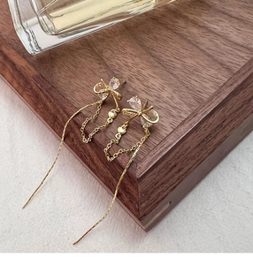Close-up of gold bow earrings with long tassel chains and tiny heart pendants