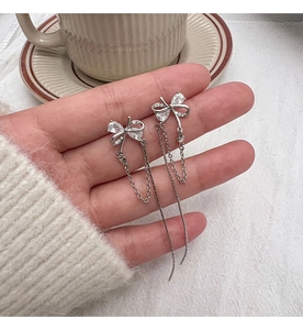 Detailed macro of silver bow earrings with asymmetrical zircon fringe held by hand