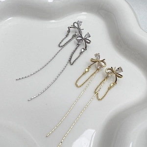 Macro shot of gold and silver bow tassel earrings with zircon stones on white ceramic