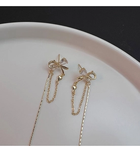 Detail of gold bow tassel earrings with zircon waterdrop on a white porcelain plate