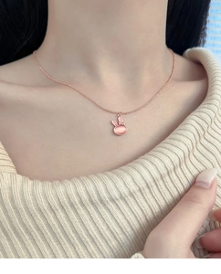 Close-up of rose gold rabbit necklace featuring a pink cat eye stone on a model wearing beige