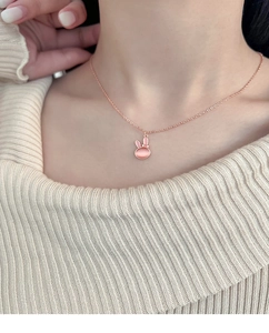 Close-up of pink cat eye stone rabbit pendant on a rose gold chain with knit sweater