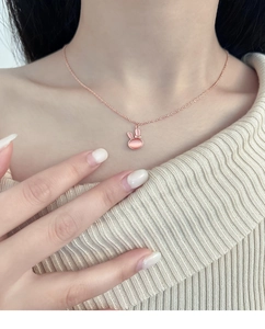 Close-up of pink cat eye stone rabbit pendant on a rose gold necklace worn by a model