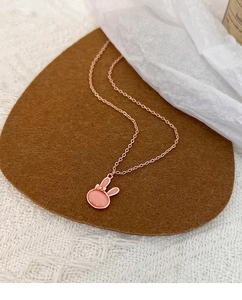 Close-up of pink opal rabbit pendant necklace with rose gold chain on soft fabric