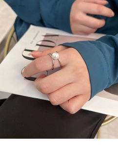 Detail of elegant cross-band silver ring featuring a large lustrous white pearl on a finger