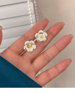 Gros plan de boucles d'oreilles gardénia argentées avec centre doré à la main
