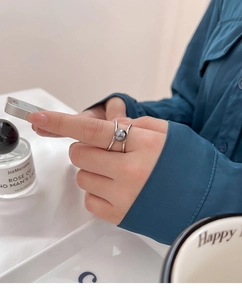 Close-up of a silver criss-cross pearl ring featuring a grey pearl on a model's hand