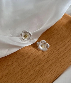 Détail macro de boucles d'oreilles gardénia argentées sur de la soie et du bois