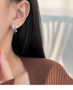 Detail view of a silver bow earring with sparkling zircon tassel on a female model