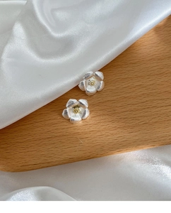 Détails de boucles d'oreilles gardénia argentées avec centre doré sur soie blanche