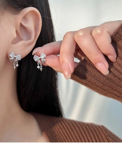 Close-up of silver bow earrings with sparkling star charms and zircons on model ear
