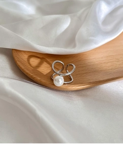 Macro shot of silver pearl ring with dual-layer cross design on wooden tray