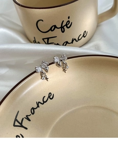 Detailed view of silver bow earrings with sparkling zircon stars on a ceramic saucer