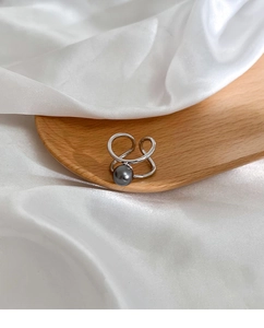 Detailed view of an elegant silver open ring with a deep grey pearl on silk fabric