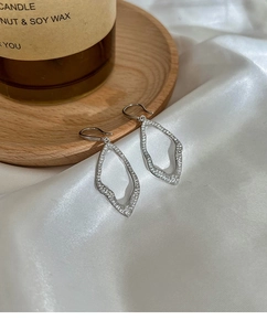 Detailed view of silver geometric teardrop earrings with crystals on white silk fabric