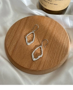 Detailed macro shot of irregular geometric silver zircon earrings on wooden stand