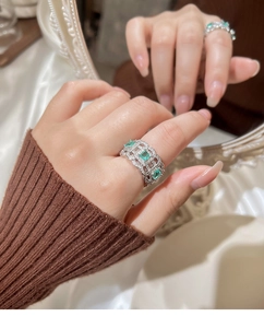 Detailed shot of vintage hollow-out ring with emerald green stones on model hand