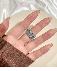 Close-up of a hollowed silver ring featuring three emerald-cut green gemstones on model's hand
